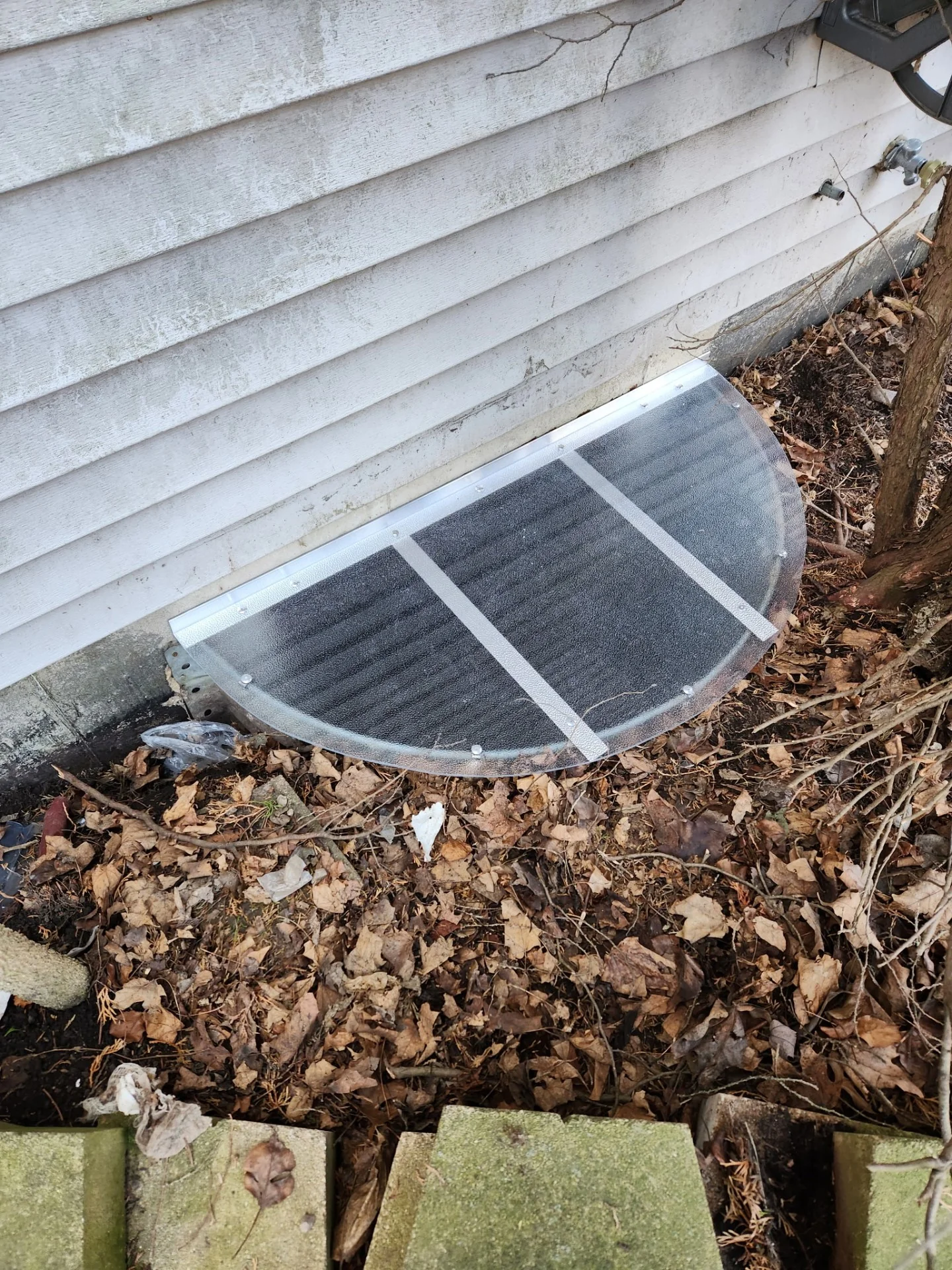 Half-round window well cover on white vinyl-sided home in fall