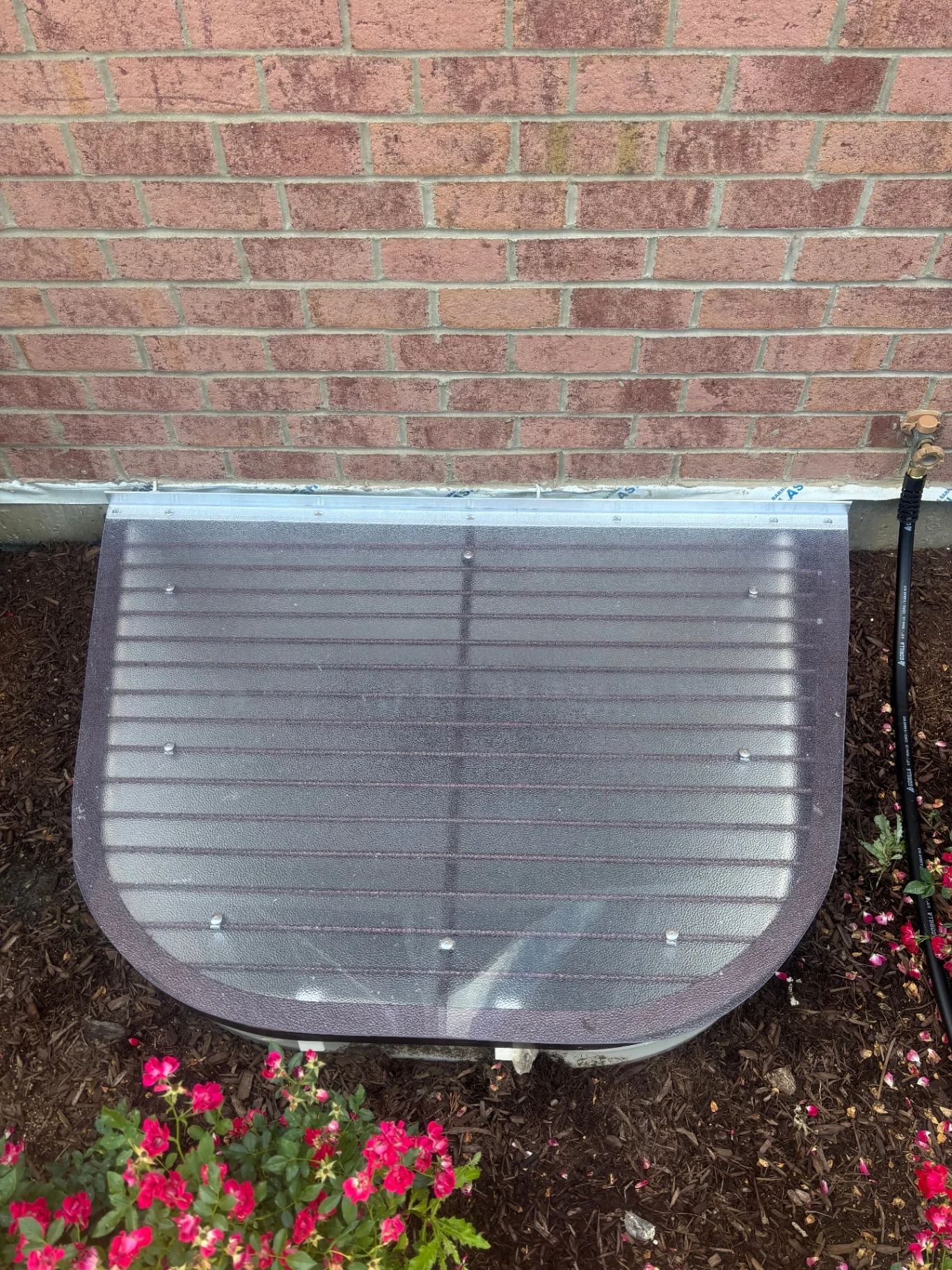 Large egress window well cover with aluminum frame on brick home