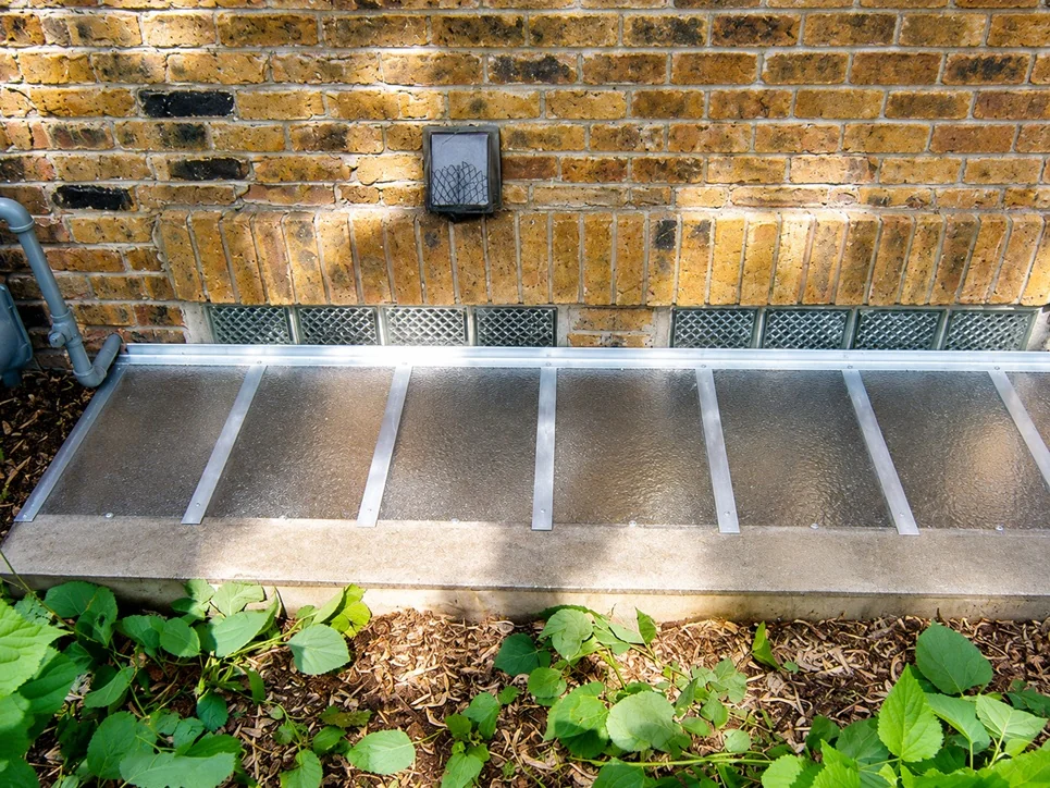 Long custom cover over glass block basement window on yellow brick home