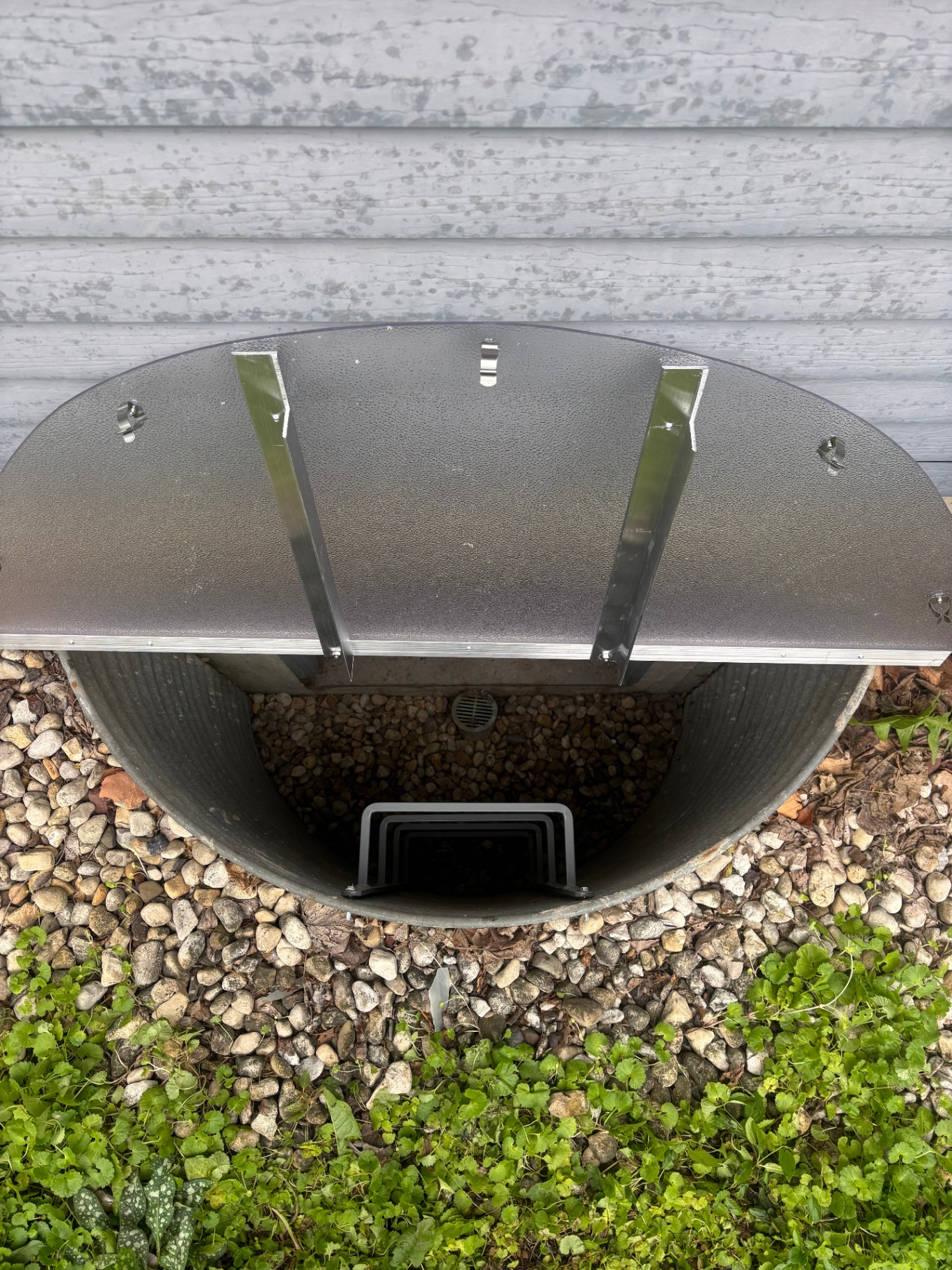 Open galvanized window well with black egress ladder and gravel bottom