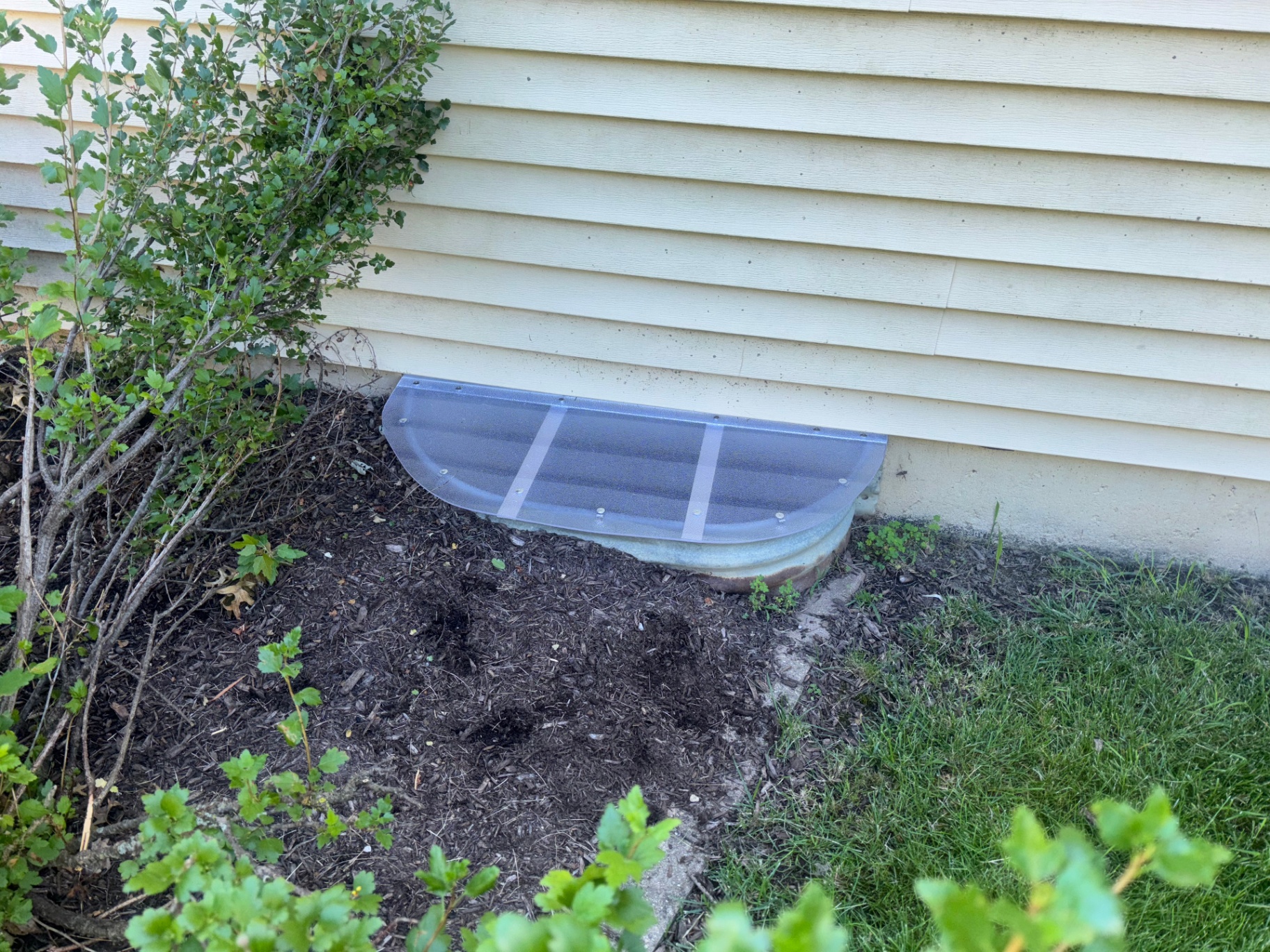 Custom half-round window well cover on galvanized well by cream vinyl siding