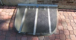 Small tinted window well cover installed on brick paver patio
