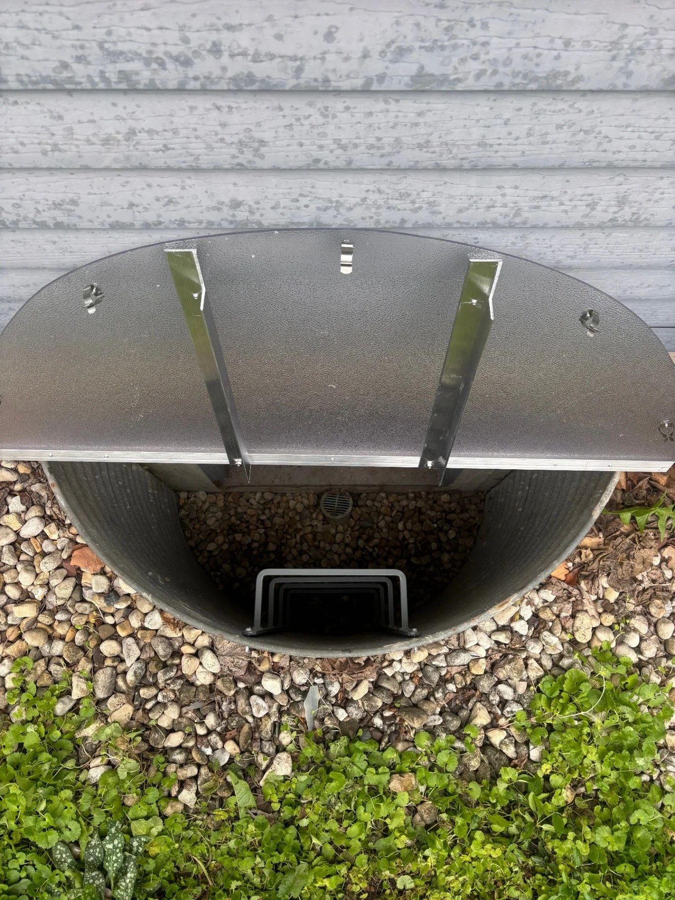 Open galvanized window well with black egress ladder and gravel bottom