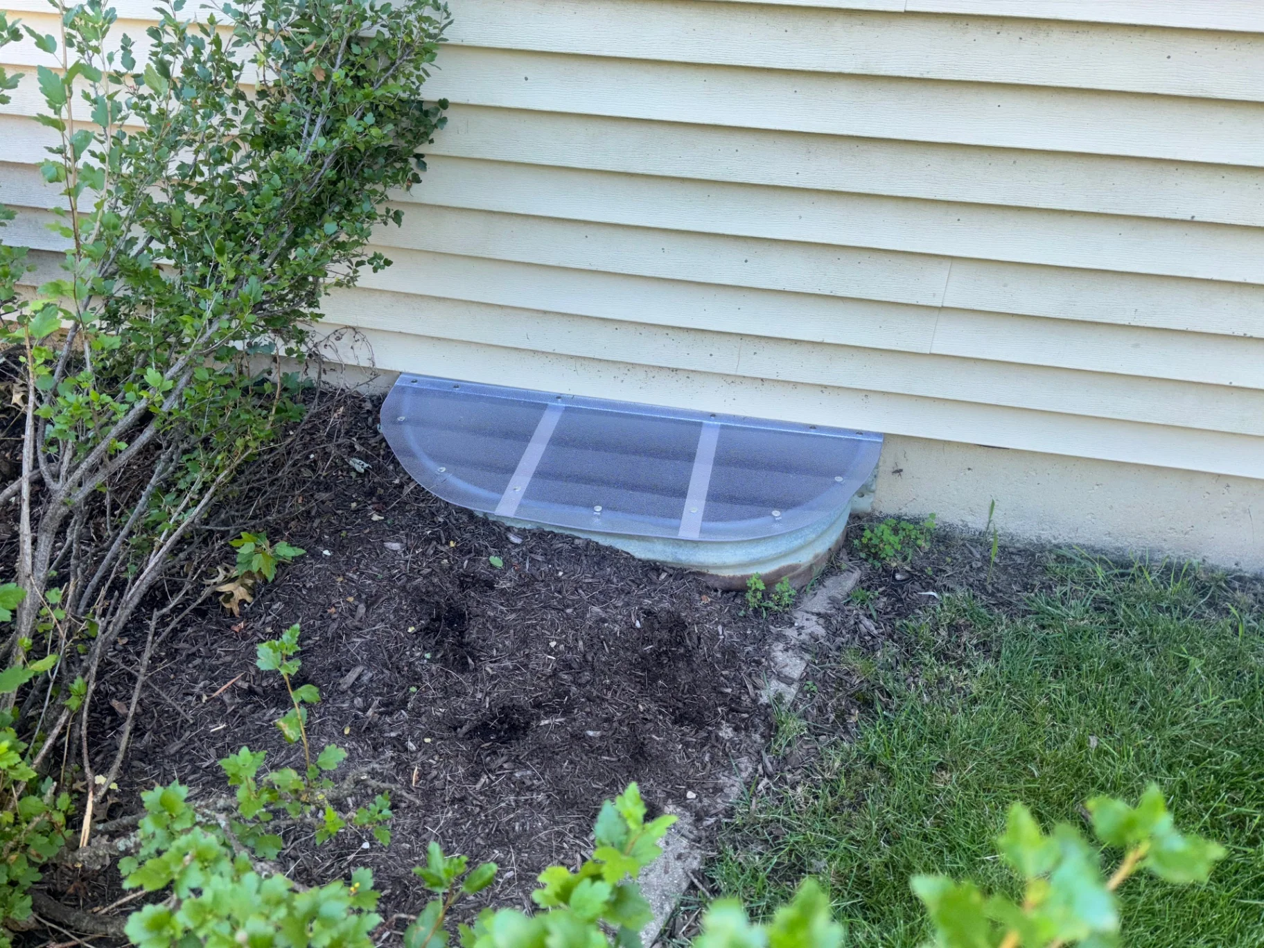 Custom half-round window well cover on galvanized well by cream vinyl siding