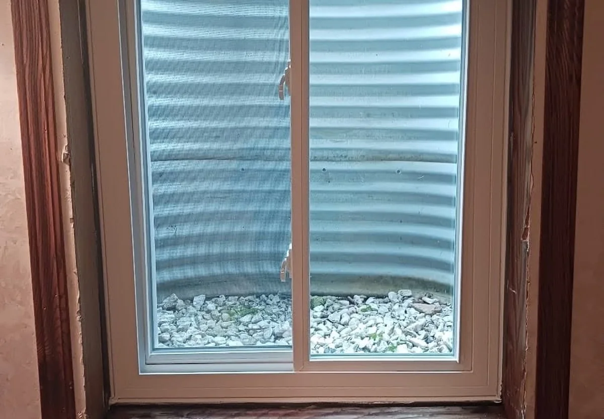New basement replacement window with wood trim and a clean rock-filled window well outside