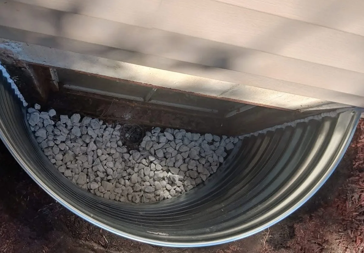 Newly installed galvanized window well filled with clean drainage rock and a center drain
