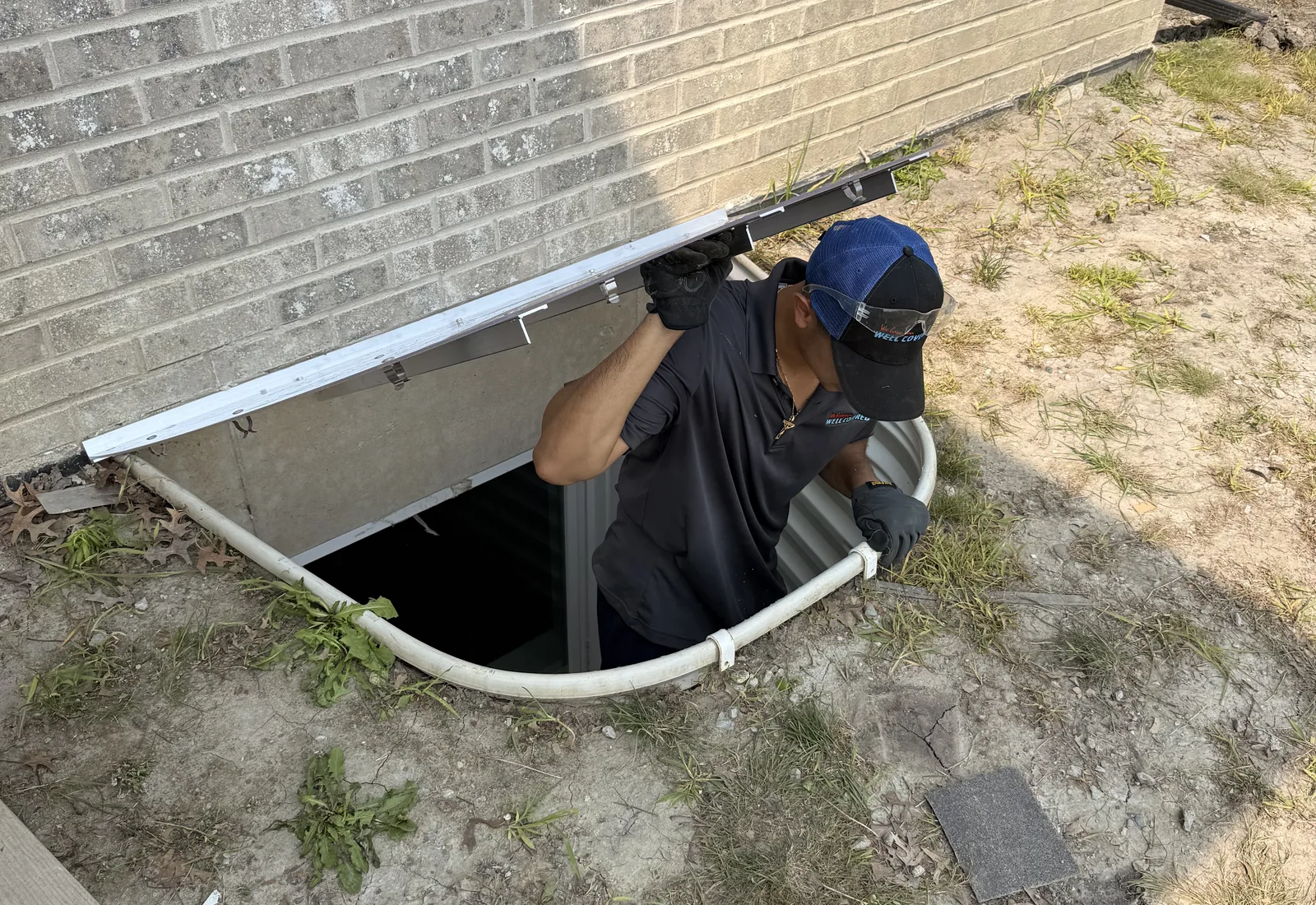 Well Covered technician lifting the cover as he climbs out of a code-compliant egress window well